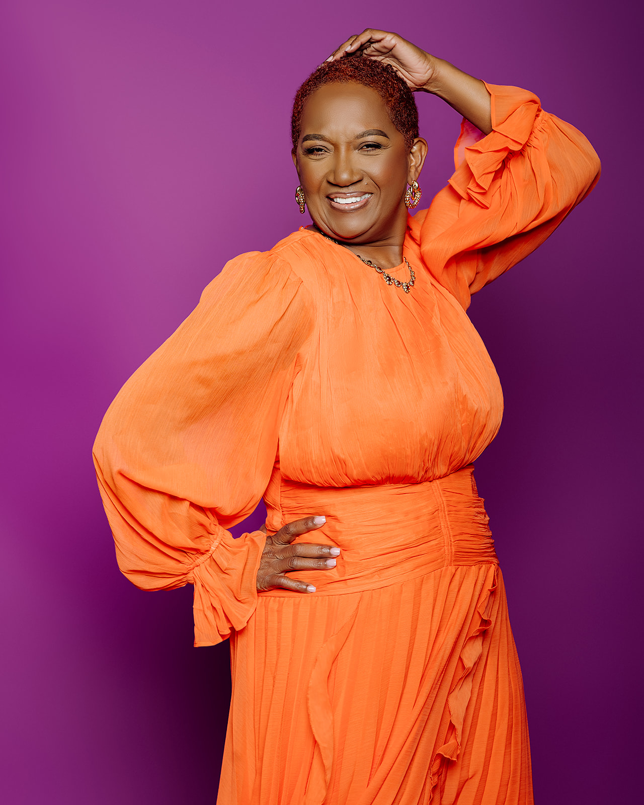 60th birthday studio portrait in orange dress on purple backdrop
