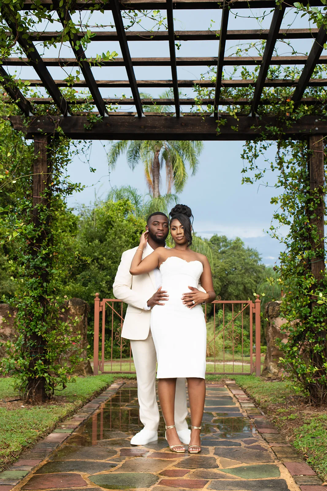 Engaged couple in cream and white under vine-covered pergola