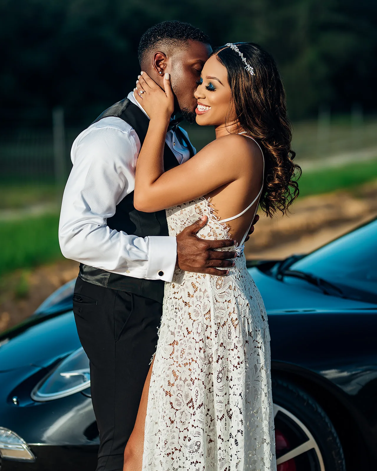 Couple kissing beside luxury car in lace dress