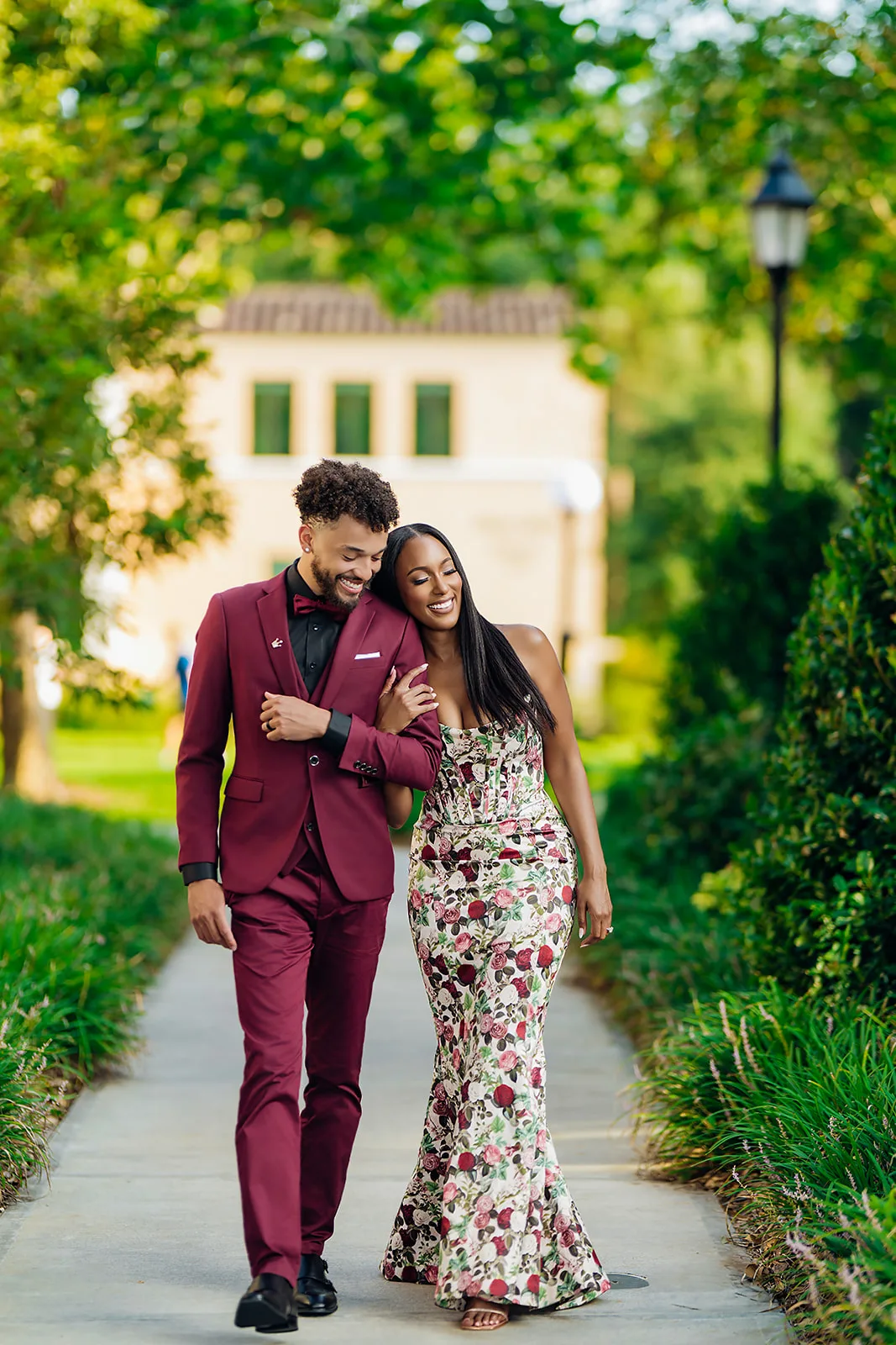 Playful engaged couple walking a tree-lined path in formalwear