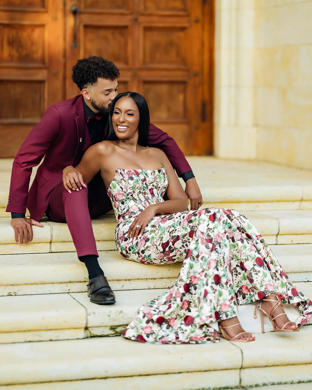 Romantic couple seated on stone steps in floral gown and burgundy suit