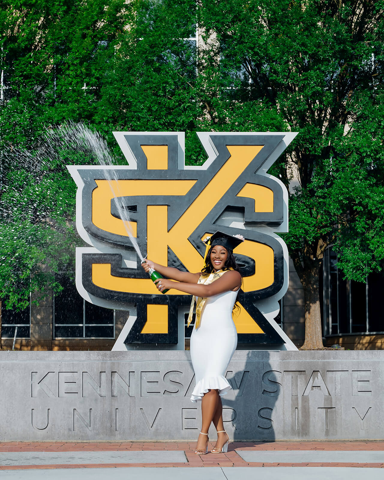Kennesaw State University graduate spraying champagne in front of KSU logo