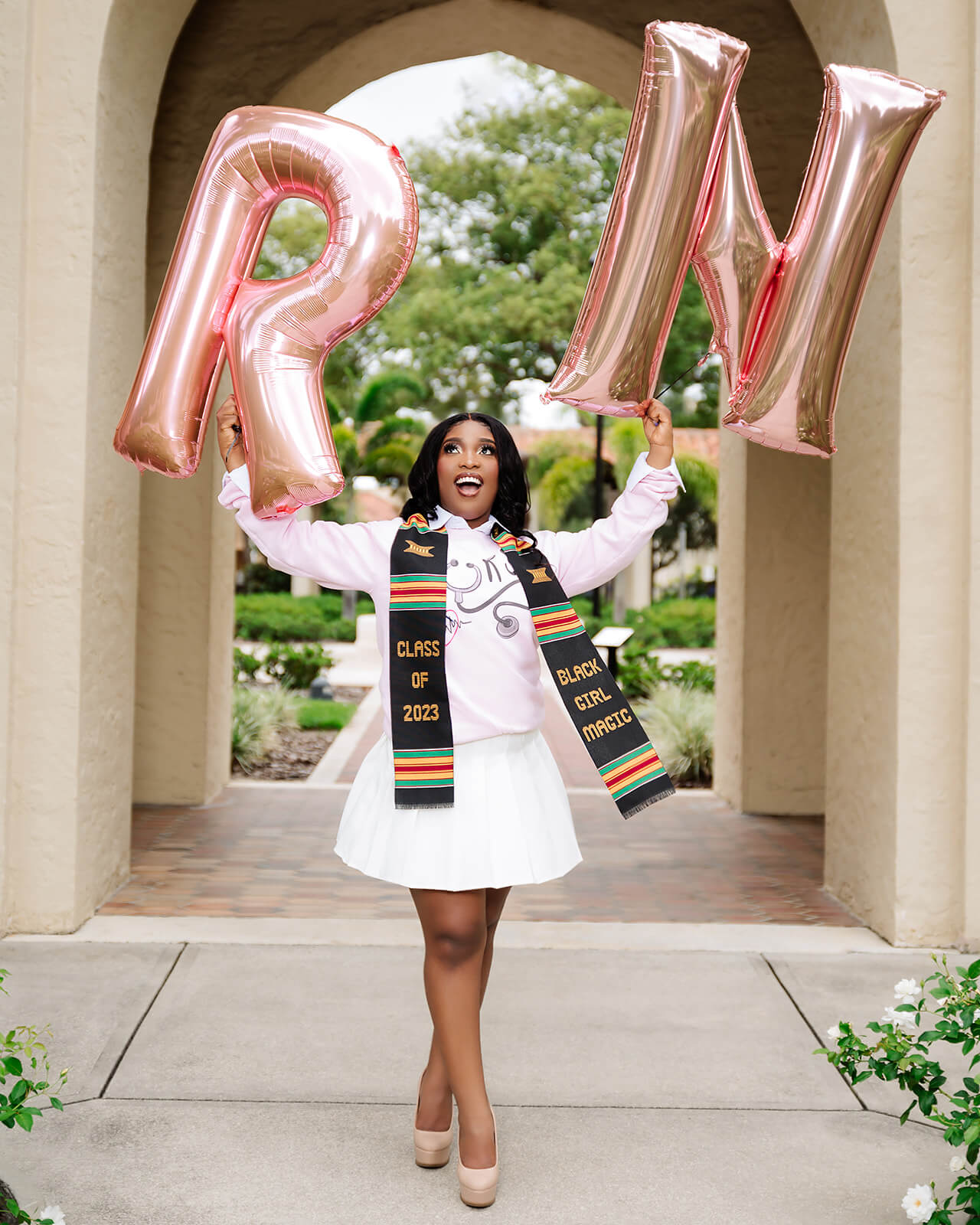 Nursing graduate with rose gold RN balloons and kente Black Girl Magic stole
