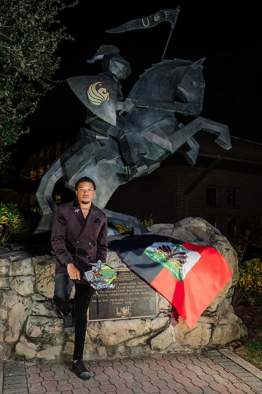 UCF engineering graduate with Haitian flag in front of Knight statue at night