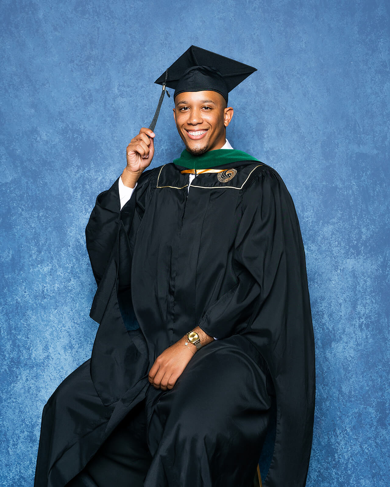 UCF masters graduate seated portrait in cap and gown on blue backdrop