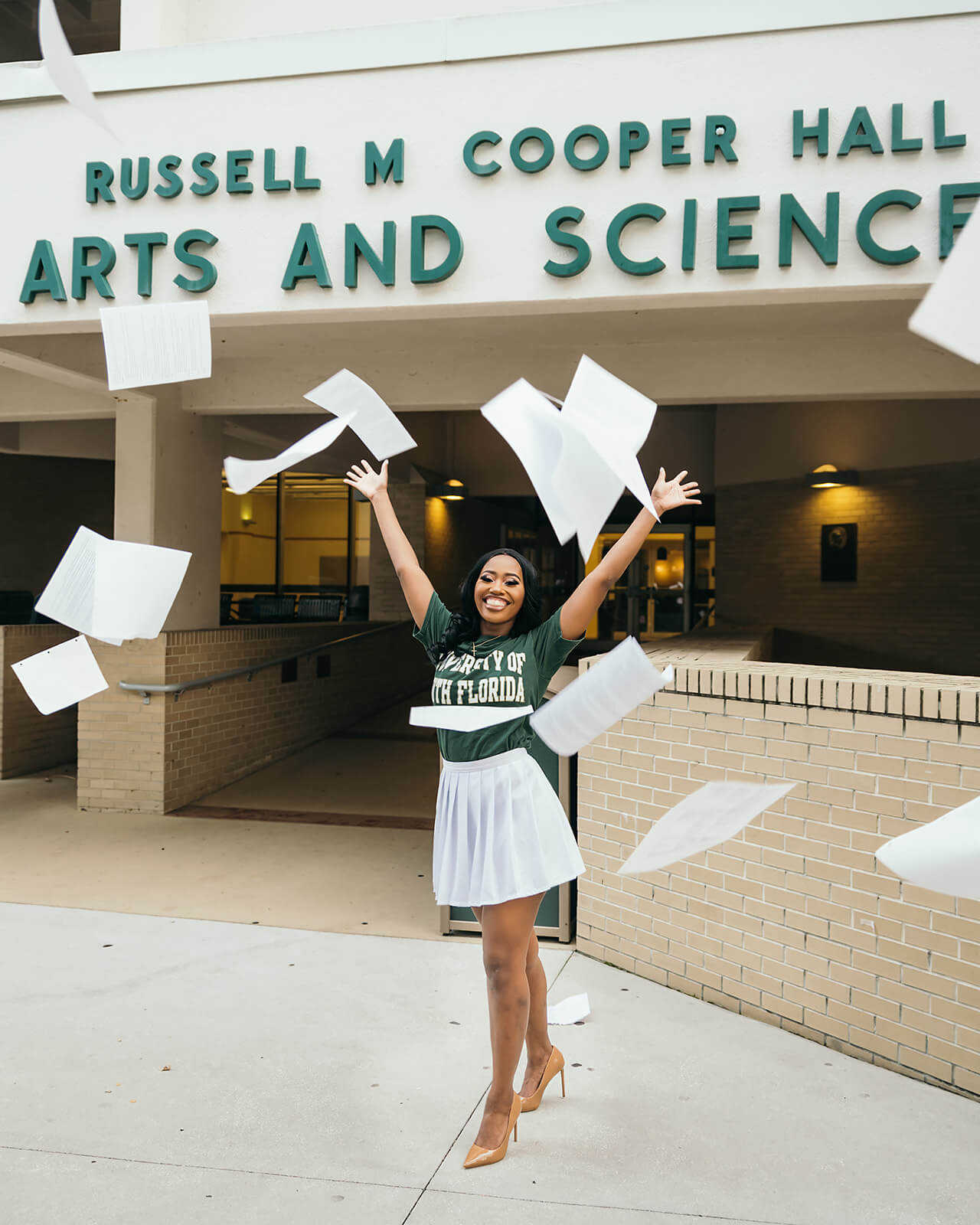 USF graduate tossing thesis papers outside Russell M Cooper Hall arts and sciences
