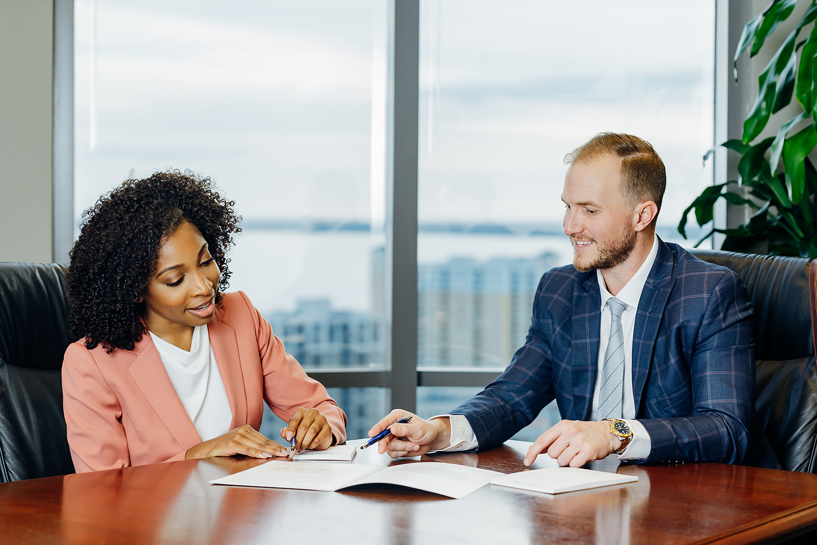 Two professionals in a high-rise office meeting with skyline view