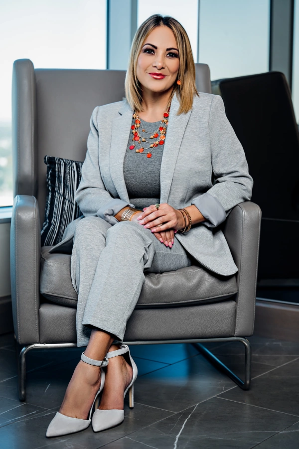Seated executive headshot of a woman in a grey suit by a city window