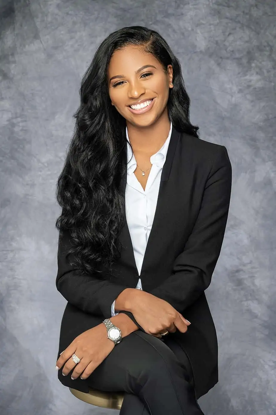 Studio headshot of a woman in a black blazer on grey backdrop