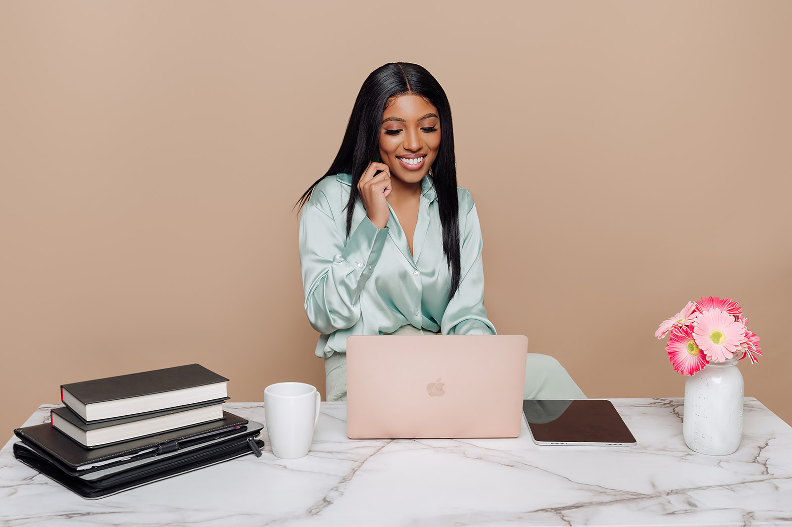 Woman in mint silk shirt smiling at rose gold laptop on marble desk