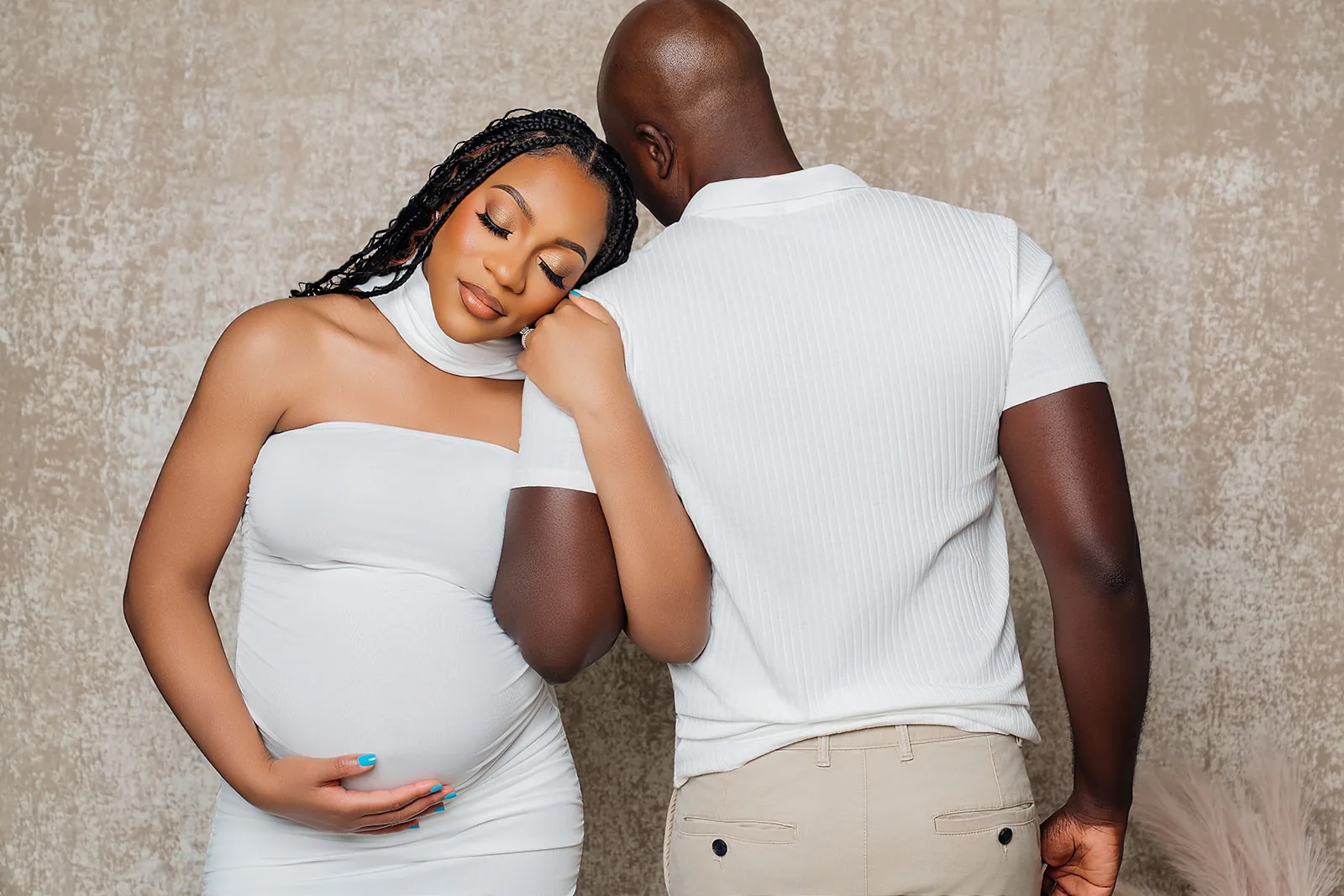 Maternity couple portrait — partners in white on tan textured backdrop