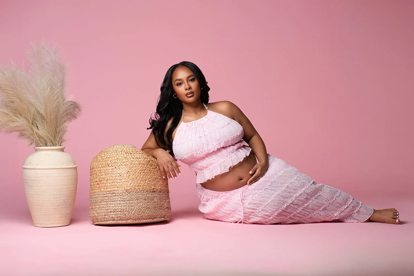 Maternity portrait — expecting mother in pink ruffled set on pink backdrop