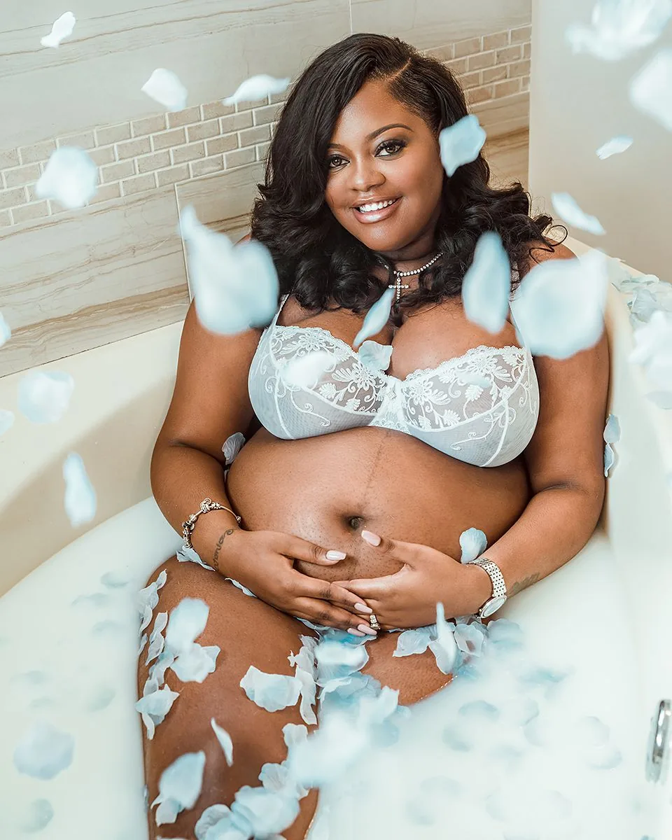 Maternity portrait — expecting mother in white lace with floating blue rose petals in tub