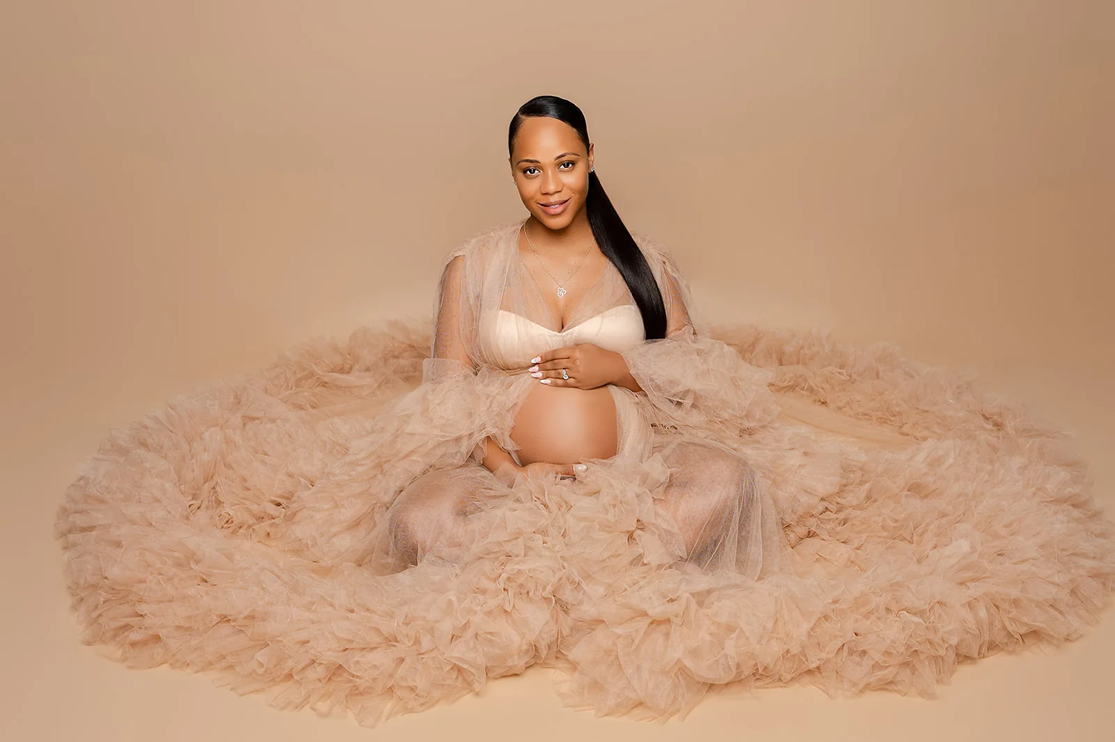Maternity portrait — expecting mother seated in nude tulle gown