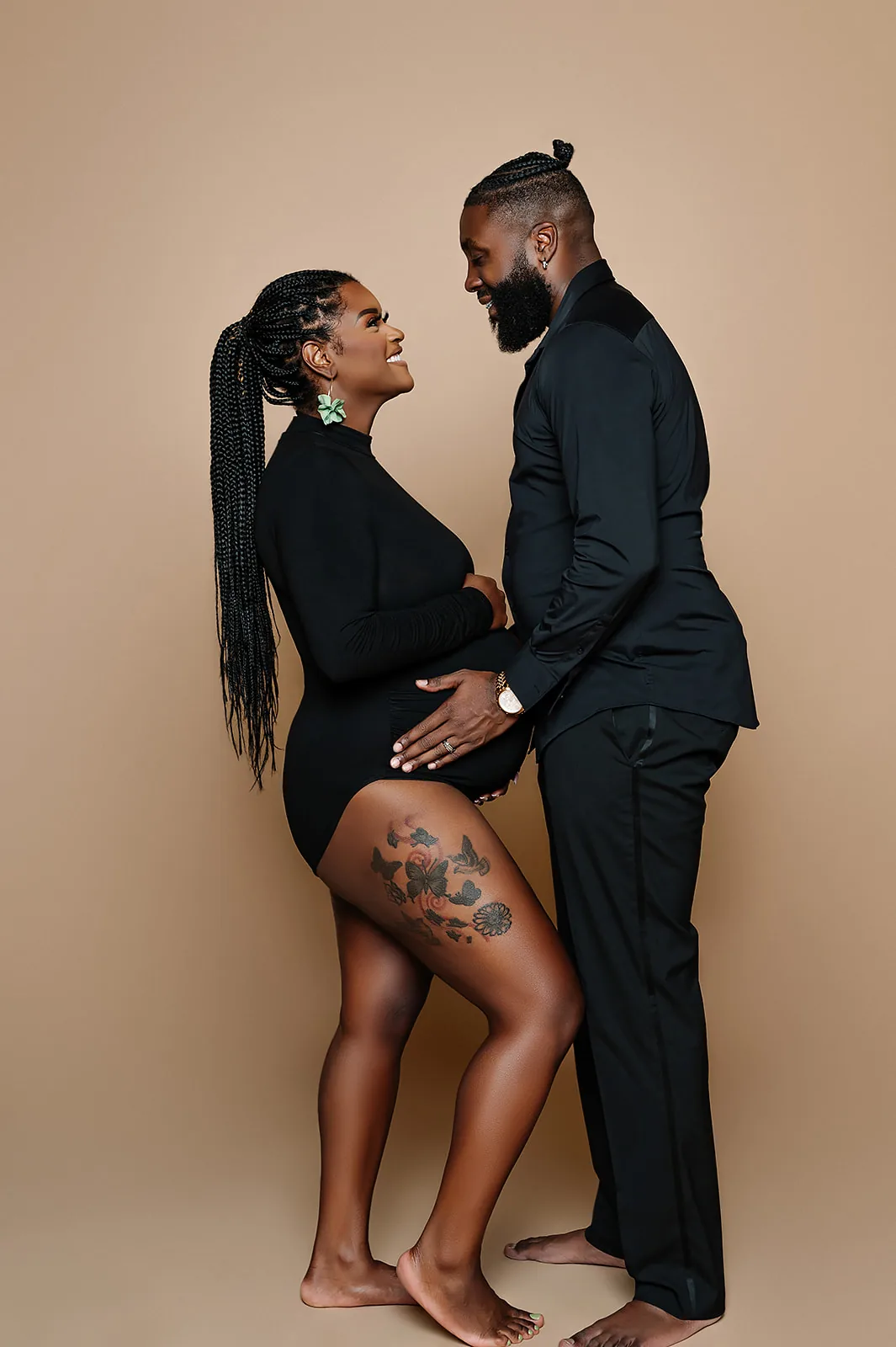 Maternity couple portrait — partners in black on tan backdrop