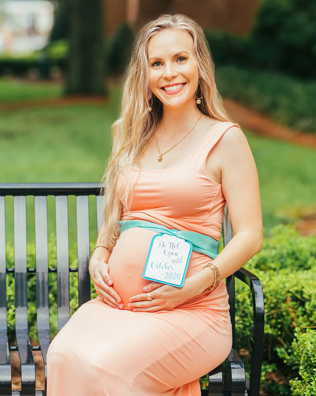 Maternity portrait — expecting mother in peach dress seated on garden bench