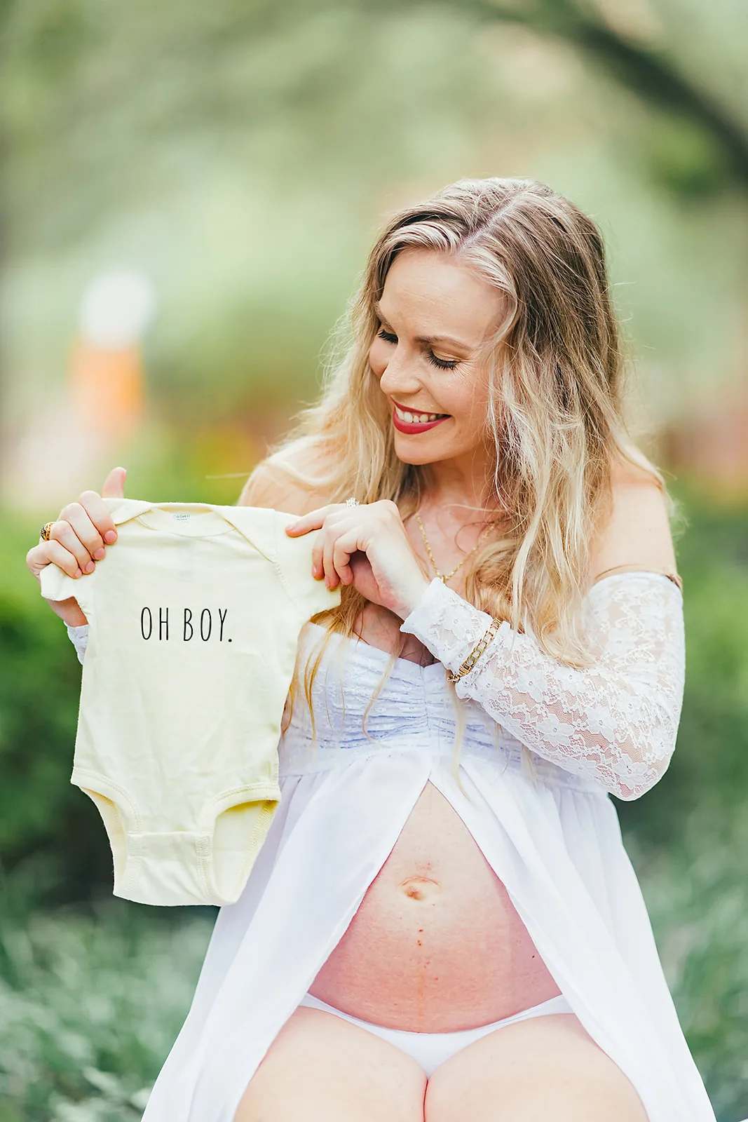 Maternity portrait — expecting mother holding Oh Boy onesie outdoors