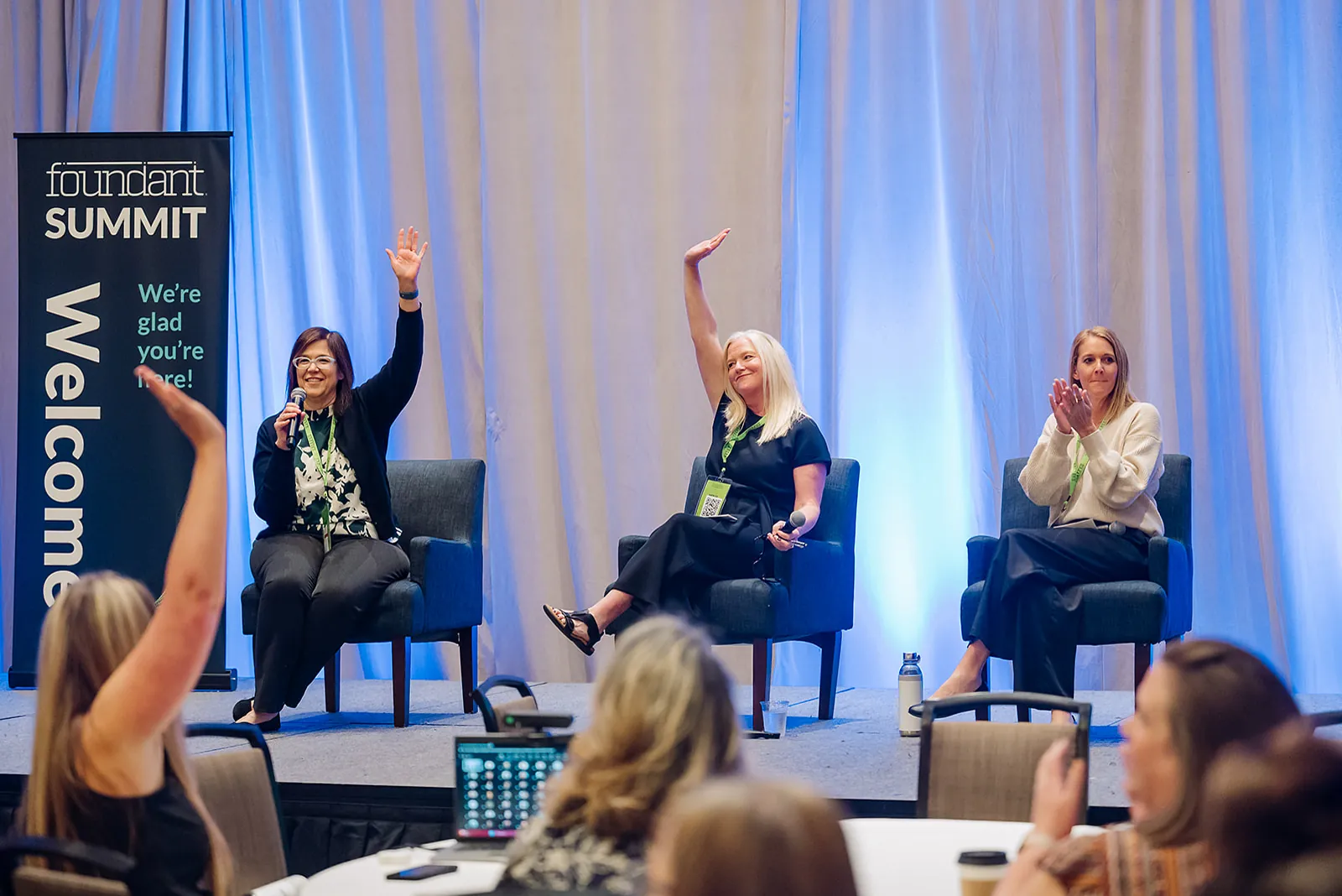 Three panelists on stage raising hands during a Foundant Summit panel discussion in Tampa