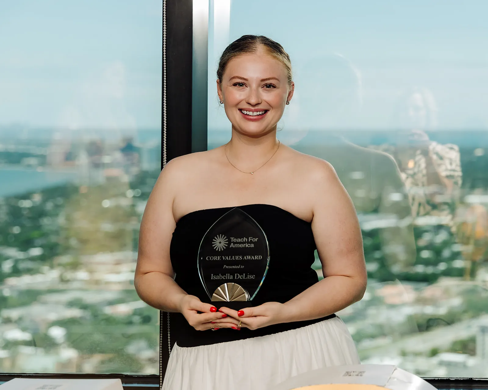 Teach For America Core Values Award recipient holding her award with the downtown Tampa skyline behind her