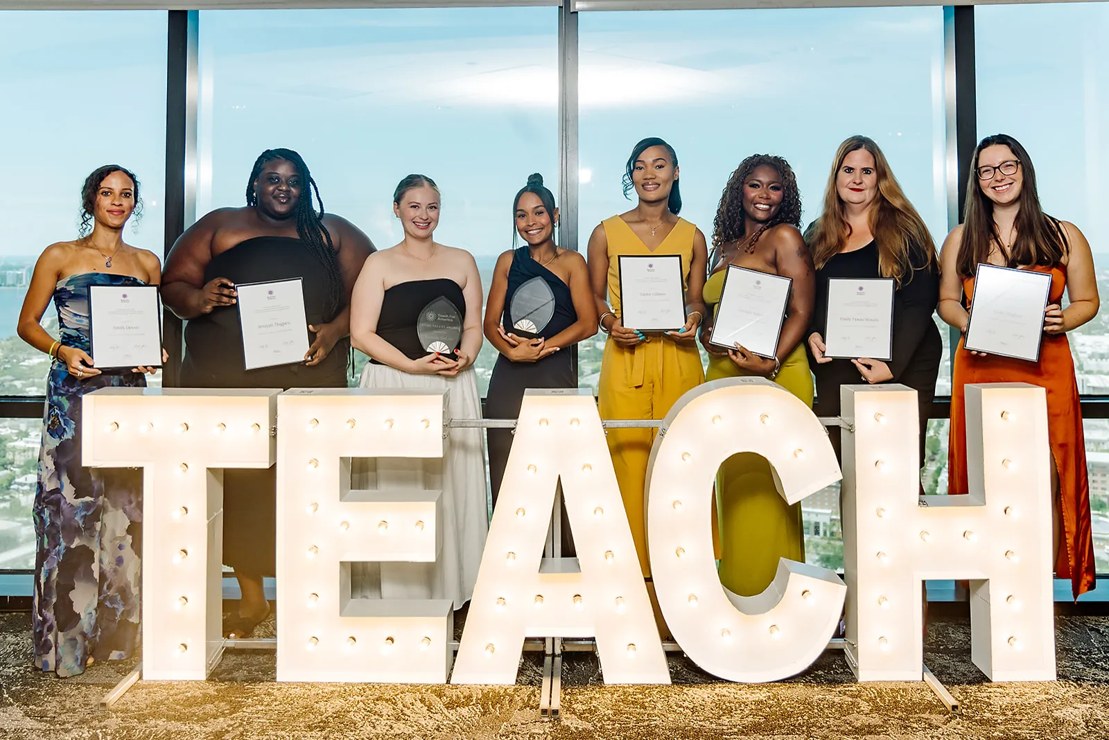 Teach For America Core Values Award recipients posed behind illuminated TEACH marquee letters with the Tampa skyline in the background