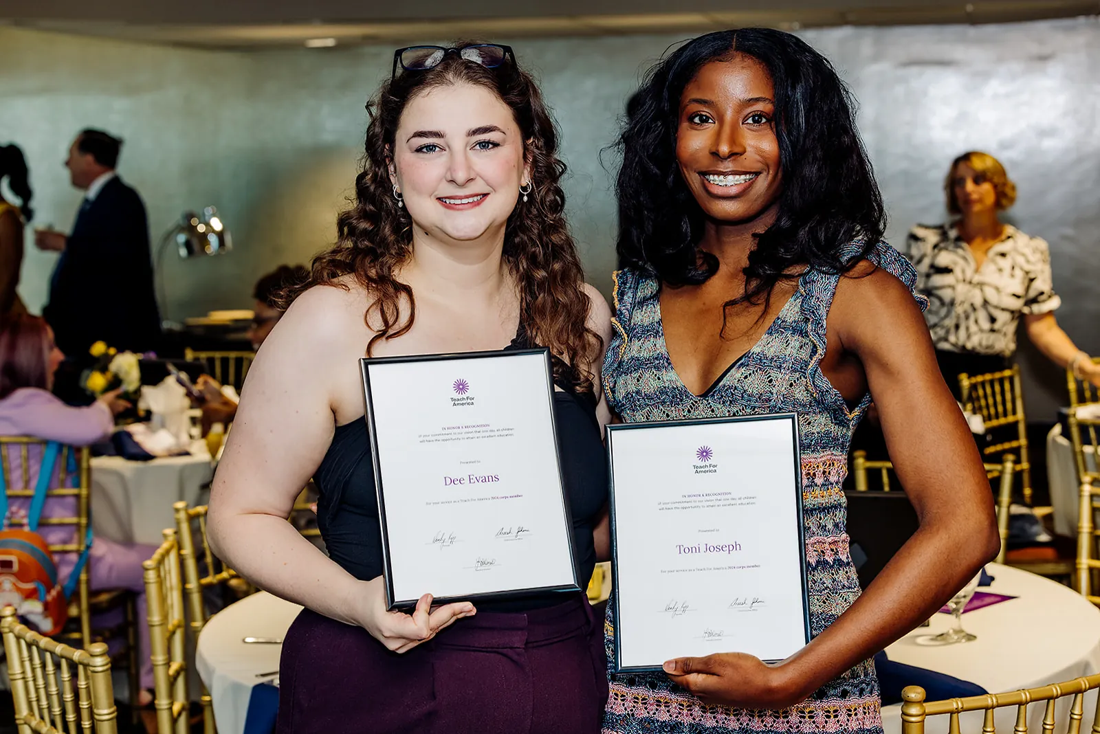 Two Teach For America 2024 corps members smiling with framed recognition certificates at the Tampa ceremony