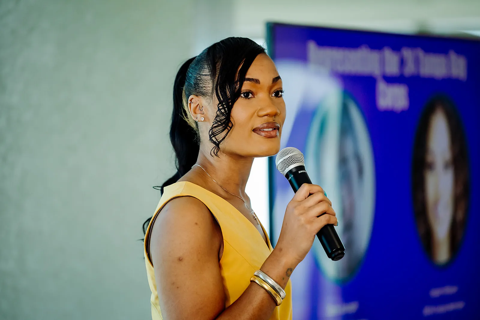 Teach For America speaker in a yellow dress addressing the audience with a microphone at a Tampa event