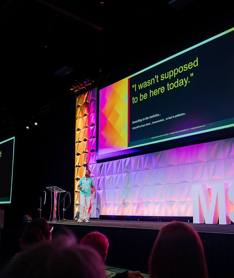Keynote speaker on a convention main stage with large projection screens behind them