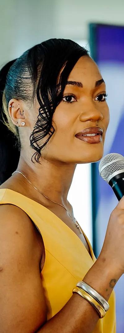 Teach For America speaker in a yellow dress addressing the audience with a microphone at a Tampa event